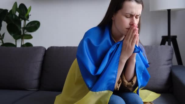 伤心忧郁的年轻女子被笼罩在乌克兰国旗下 一个人坐在家里的沙发上 吓坏了 停止俄罗斯和乌克兰之间的战争 和乌克兰呆在一起为和平与世界祈祷和希望 — 图库视频影像