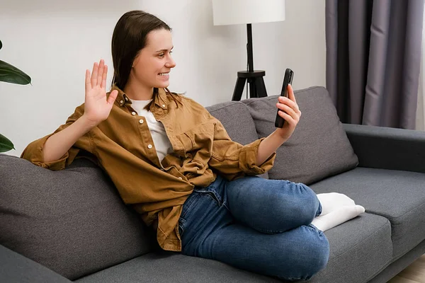 Smiling Young Female Sitting Couch Waving Hand Using Smartphone App — Stock Photo, Image