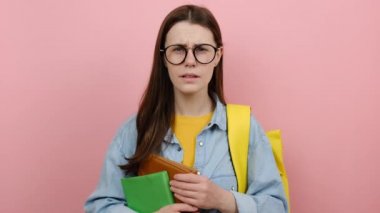 Genç kız öğrencinin portresi gömlek giyer ve sarı sırt çantalı kitaplarda gözlük takar. Stüdyodaki pembe renkli arka plan duvarına izole edilmiş poz verir. Üniversite konsepti eğitimi