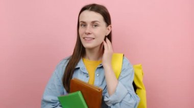 Meraklı, gülümseyen, eğlenceli kızın portresi tişört ve sarı sırt çantalı kitaplar giyer. Kulak misafiri olmaya çalış.