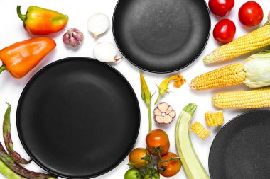 Sonbahar sebzelerinden yapılmış yaratıcı bir düzen. Domates, soğan, havuç, sarımsak, kırmızı pancar, biber, kabak, mısır, yeşil kayısı ve beyaz stüdyo arka planında siyah tabak. Düz konum, üst görünüm, kopyalama alanı