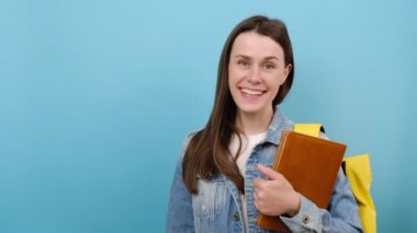 Promosyoncu kız 20 'li yaşlarda kot ceket giyiyor ve sarı sırt çantalı kitaplar çalışma alanının fotokopisini çekiyor. Stüdyodaki pastel pembe arka planda izole edilmiş poz veriyor.