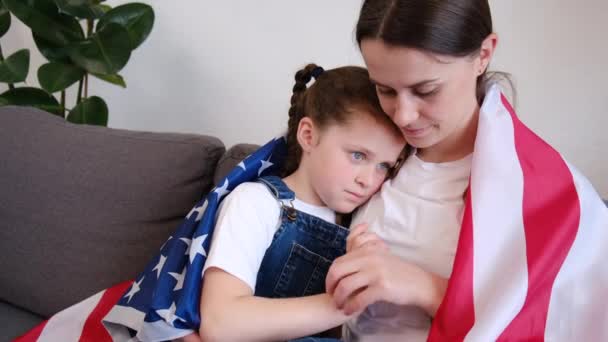 愛国的なかわいい若い母親と美しい小さな娘の子供は家で居心地の良いソファに座ってアメリカ国旗を保持しています 誇り高い独立した家族の自由を感じ 独立したコンセプトを笑顔 — ストック動画