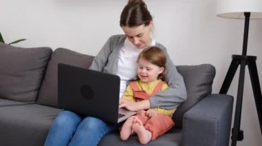 Mutlu genç anne ve tatlı kız online alışveriş yaparken rahat koltukta otururken, gülümseyen anne küçük kıza dizüstü bilgisayar uygulamasını öğretirken, çizgi film izlerken ya da bilgisayar başında video görüşmeleri yaparken.