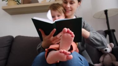 Mutlu ailenin seçici odağı genç anne kitabı oku rahatla küçük kızı kucakla, gülümse anne küçük çocuğa komik bir masal anlat rahat kanepeye otur ve evde birlikte eğlenelim.