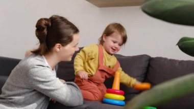 Sevgi dolu anne ve tatlı kızın evdeki rahat gri koltukta plastik oyuncaklarla öğrenme oyunları oynaması, çocuk gelişimiyle ilgilenmesi. Neşeli genç anne, tatlı küçük kız çocuğuyla ayrılışı kutluyor.