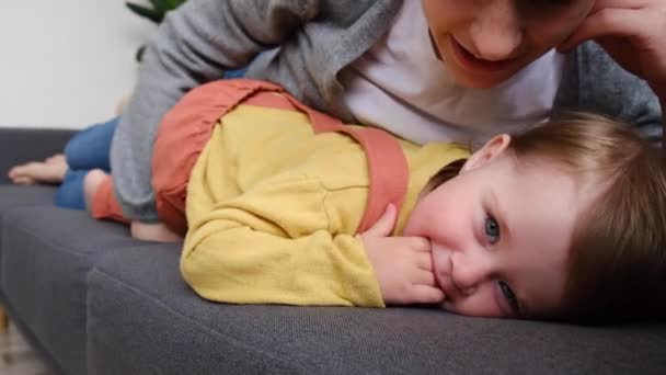 Szczęśliwy Kochający Młody Matka Piggyback Leżący Kanapie Całuje Słodkie Dziecko — Wideo stockowe
