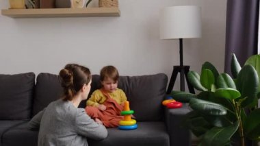 Anne ve kızını sevmek evdeki rahat koltukta plastik oyuncaklarla oyun oynamak. Neşeli genç anne, tatlı küçük kız çocuğuyla ayrılışı zevkle yapıyor. Mutlu aile, annelik ve çocukluk eğlencesi
