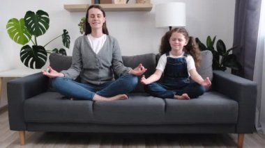 Annem gibi yapıyorum. Sakin bir anne ve küçük kızı, modern stüdyo dairesindeki rahat koltukta birlikte yoga yaparak bacak bacak bacak üstüne atarak eğleniyor. Komik küçük kız annesini meditasyon yaparken taklit ediyor.