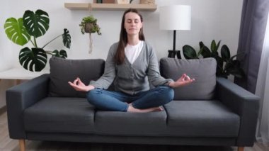 Stres yok, denge konsepti. Sakin, genç, beyaz bir kadın oturma odasındaki rahat koltukta bacak bacak üstüne atarak oturur. Gözler kapalı meditasyon yapar. İç ahengi hisseder, bilinci ve farkındalığı geliştirir.