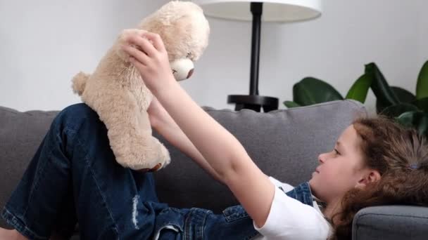 Χαμογελώντας Χαριτωμένο Κοριτσάκι Χαλαρώνοντας Άνετο Καναπέ Αγκαλιάζοντας Αρκουδάκι Αίσθημα Αγάπης — Αρχείο Βίντεο