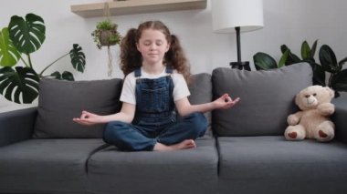 Sağlıklı, küçük, çekici bir çocuğun yoga egzersizi yapması, evdeki rahat koltukta pofuduk bir ayının yanında oturması, güzel, sakin, küçük bir kızın aile meditasyonunu öğrenmesi, rahatlaması konsepti gevşetmesi.