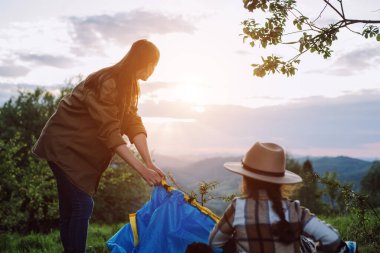 Yürüyüşçü genç anne ve kızının muhteşem günbatımında arka plandaki dağlarda çadır kurmalarının seçici odak noktası. Yaz kampı. Gezgin çadır elementlerini ayarlıyor. Seyahat ve seyahat kavramı