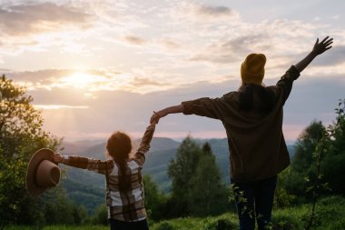Mutlu bir aile, gün batımında ya da gün doğumunda küçük kızı olan eğlenceli genç bir anne yürüyüş sonrası güzel yaz dağlarının tadını çıkarıyor. Samimi duygular ve açık havada aktif eğlence kavramı