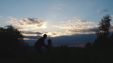 Arka plandaki yaz dağlarında küçük kızını kusan genç bir babanın silueti. Oyuncu baba ve küçük kız gün batımında sahada oynuyorlar. Baba ve çocuk birlikte eğleniyorlar. Yavaş çekim