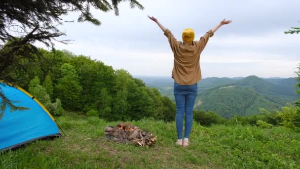 回头看 年轻的高加索女人头戴黄帽站在背景的夏山上 举起双臂 醉心于生活 青春和幸福 探索真正的野外生活方式 — 图库视频影像