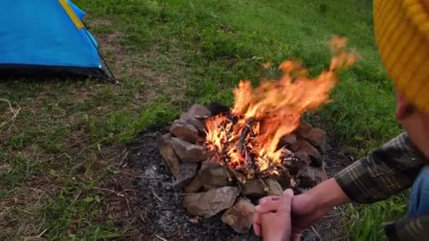 近前来远足的男青年 头戴黄帽 坐在篝火边 在山上搭起帐篷 徒步旅行后 留着胡子的旅行者在篝火边热身 生活方式概念 — 图库视频影像