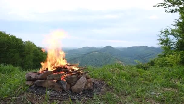 戴着黄色帽子的旅行者 徒步旅行后坐在篝火边 欣赏美丽的大自然 在夏季的高山背景下 让年轻长胡子的雄性保持冷静 流浪和生活方式概念 — 图库视频影像