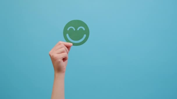 緑の幸せな笑顔の顔を保持女性の手 良いフィードバック評価と肯定的な顧客レビュー Okのサインを示します 満足度調査 精神健康評価 良い感じ 青の背景に隔離 — ストック動画