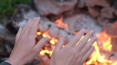 Şenlik ateşinin yanında kadın ellerini ısıtmaya yaklaş. Soğuk bir akşamda dışarıda kamp yapmak. İnsanın sıcaklığı ve sıcak atmosferi ormanda ateş yaktı. Açık hava yaşamının tadını çıkar. Seyahat konsepti. Yavaş çekim
