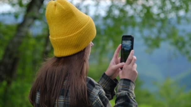 在森林里用智能手机选择性地聚焦穿针织贝尼衫的远足女孩 旅行女性徒步旅行者使用电话 女徒步旅行者用智能手机拍下群山的照片 概念探险旅行博客Wanderlust — 图库视频影像