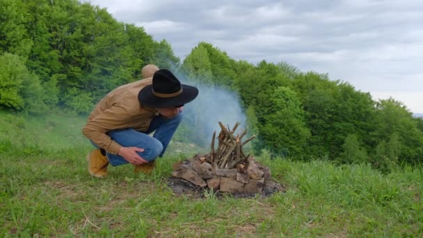 Χαλαρός Νεαρός Άνδρας Μαύρο Καπέλο Ανάβει Φωτιά Φόντο Πράσινο Δάσος — Αρχείο Βίντεο