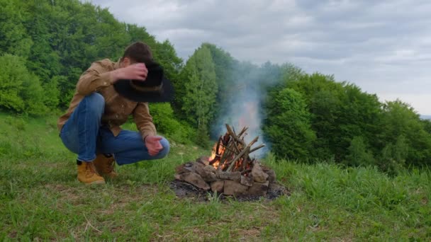 Young Bearded Man Black Hat Kindles Bonfire Background Green Forest — Stockvideo