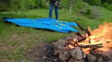 Yeşil ormandaki kamp gezisinde kamp ateşi yanında kamp kuran örgü bereli genç bir kadının seçici odak noktası. Kamp ateşiyle yaz kampı. Gezgin çadır elementlerini ayarlıyor. Seyahat tutkusu konsepti