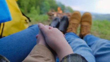 Romantik kamp kavramı. Yaz günü kamp ateşinin yakınındaki mavi çadırda el ele tutuşan çiftlerin seçici odak noktası ormanda akşam huzuru ve uyumu. Seyahat tutkusu konsepti