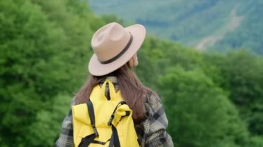 Güzel esmer kadın gezgin sarı sırt çantası ve şapka takıyor, güzel doğanın tadını çıkarıyor, atmosferik destansı anın. Genç kuşaklar için macera kaçamağı ve açık hava yaşam tarzları