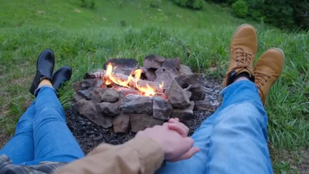 无法辨认的男女青年手牵手躺在篝火和森林的背景图上 无忧无虑的游客露营 一边欣赏大自然 一边玩弄着他们的手指 一边观看着火光 — 图库视频影像