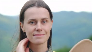 Çekici beyaz bir kadının yakın plan portresi kameraya bakıp gülümseyen, yaz günü arka plandaki dağlarda poz veren şapkalı genç ve güzel bir kız. Seyahat, macera ve seyahat tutkusu konsepti