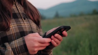 Close-up of female hands using smartphone standing of background summer mountains at evening time. Social networks Navigator and messenger. Use your mobile phone for walk in woods. Hiking concept