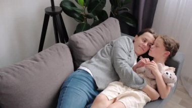 Loving young mother cuddles little daughter, family lying on comfy sofa in living room, feel unconditional love show devotion, express caress. Caring mom, adopted kid, Mothers Day celebration concept