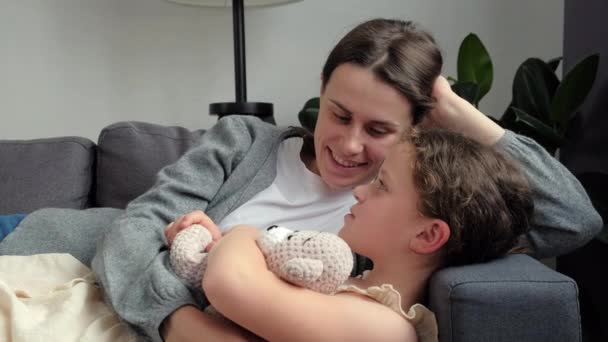 Close Loving Mother Cuddles Talking Little Daughter Lying Cozy Sofa — Video Stock