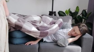 Caring little daughter covering sleepy young mom with blanket or plaid. Loving kid girl touching, comforting sleeping tired mother at home. Peaceful mommy taking nap on comfy couch in living room