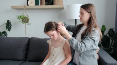 Loving caring mother brushing daughter hair sitting on cozy sofa, smiling single mom sister helping child girl with hairstyle at home getting ready, family care. Morning preparations lifestyle concept