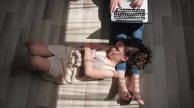 Top view of mom works at computer near little daughter plays toys. Multitasking mother works remotely at home at computer, look after kid. Problems related to working from home. Happy family concept