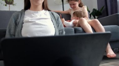 Evde dizüstü bilgisayarla uzaktan çalışma yapan sevimli bir anne. İki küçük tatlı kızın yanında oturmuş akıllı telefon oyunu oynuyorlar. Modern aile araç gereç kullanır