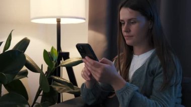 Pozitif rüya gibi genç bir kadının kanepeye oturup akıllı telefon konuşmaları, arkadaşlarıyla mesajlaşmaları, sosyal medya haberlerini yazmaları, mobil cihazlara mesaj yazmaları dokunmatik ekranlar.