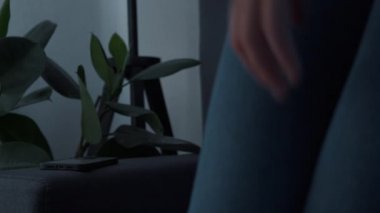 Close up of attractive young woman sitting on sofa and turning on night lamp at home, using smartphone texting with friends, scrolling social media news, writing message on mobile devices touchscreen