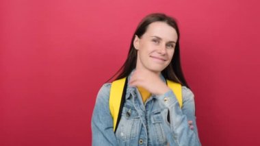 Portrait of smiling student woman 20s wearing yellow backpack standing over isolated red color background wall in studio happy looking at camera. Education in high school university college concept