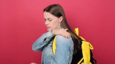 Unhealthy young brunette student woman isolated on red color background wall in studio suffering from pain in shoulder for having made an effort. Education in high school university college concept