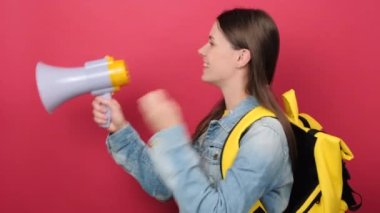 Portrait young woman student in denim jacket and yellow backpack hold scream megaphone announces discounts sale Hurry up isolated on red color background wall in studio. Education in college concept