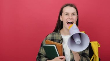 Portrait of promoter girl teen student 20s wears shirt and yellow backpack holding books scream in megaphone announces discounts sale Hurry up, posing isolated over red color background in studio