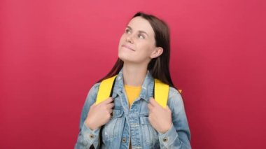 Happy young student woman with yellow backpack looking up, posing isolated over red color background wall in studio with copy space for promotion content. Education in university college concept