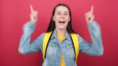 Cheerful young woman student in shirt and backpack hold index fingers up great new idea, posing isolated over red color background wall in studio. Education in high school university college concept