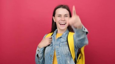 Cheerful young student woman in denim jacket and yellow backpack point index finger camera on you say do it isolated on red color background wall in studio. Education in high school college concept
