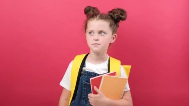 Secret little smart kid school girl with yellow backpack hold books secret say hush be quiet, finger on lips shhh gesture, posing isolated on pastel red studio background. Childhood education concept