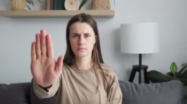 Selective focus of serious young woman showing palm to camera demonstrating stop gesture, protesting against domestic violence or abuse, struggling for female rights, racial or sexual discrimination
